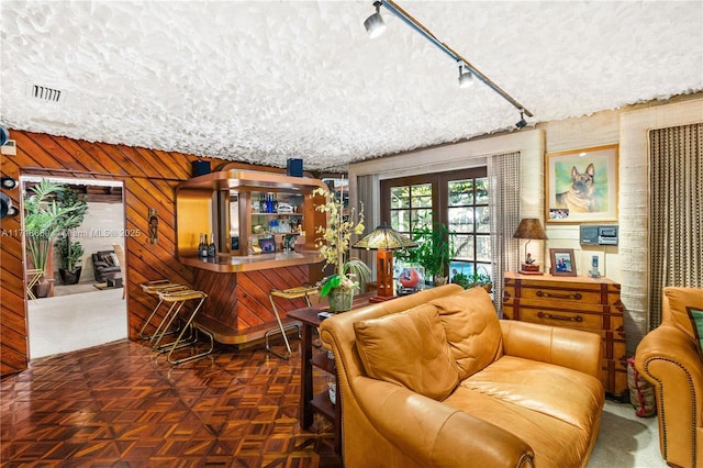 living room featuring french doors, a textured ceiling, wooden walls, and track lighting