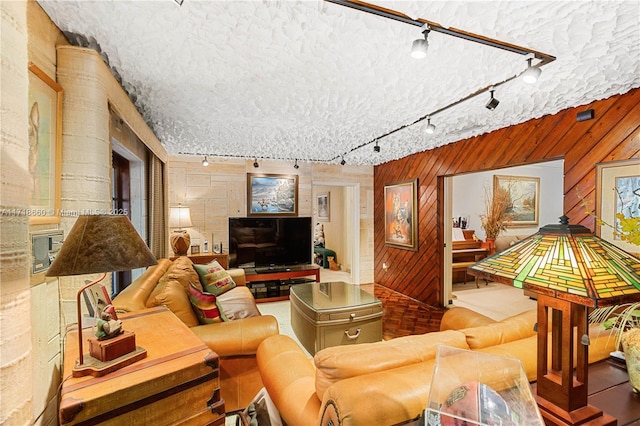 living room featuring a textured ceiling, rail lighting, and wooden walls