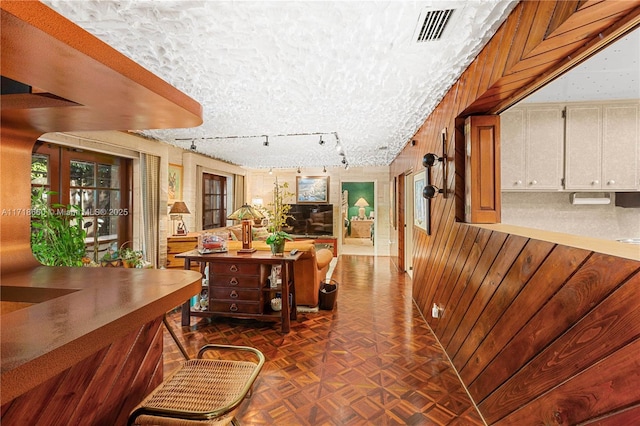 interior space with dark parquet flooring, a textured ceiling, wooden walls, and track lighting