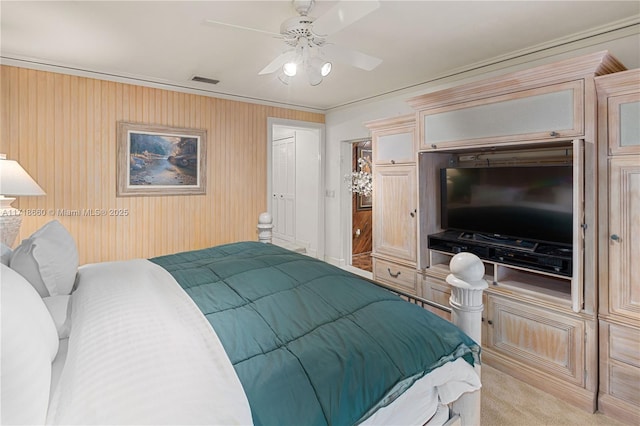 carpeted bedroom featuring wooden walls, ceiling fan, and crown molding