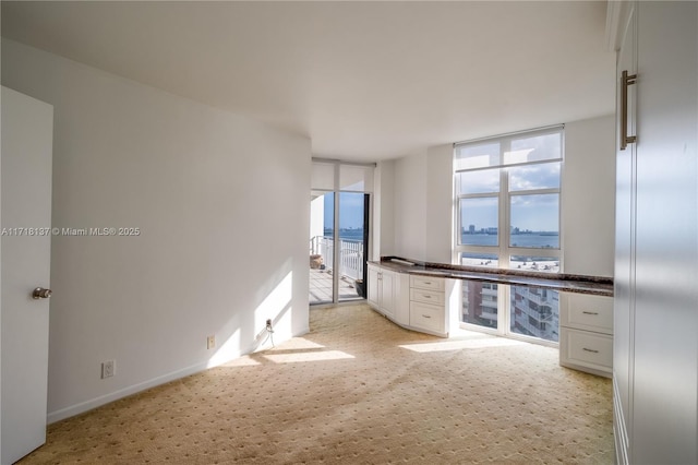 kitchen with light colored carpet, expansive windows, a water view, and white cabinetry