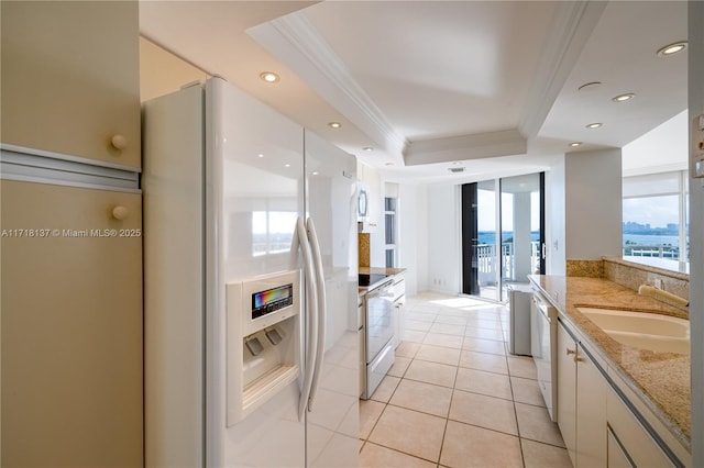 kitchen featuring light stone counters, white appliances, a raised ceiling, crown molding, and white cabinetry