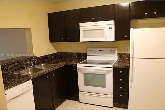 kitchen with sink, dark stone countertops, white appliances, dark brown cabinets, and light tile patterned flooring