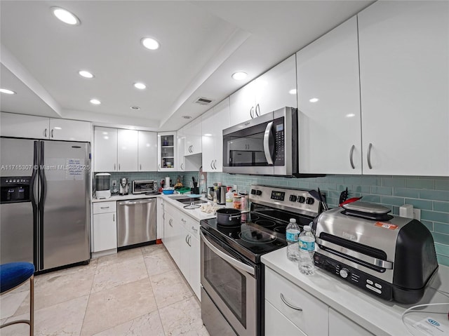 kitchen featuring sink, a raised ceiling, decorative backsplash, white cabinets, and appliances with stainless steel finishes