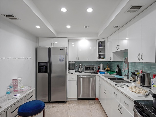 kitchen featuring white cabinetry, sink, stainless steel appliances, a raised ceiling, and decorative backsplash