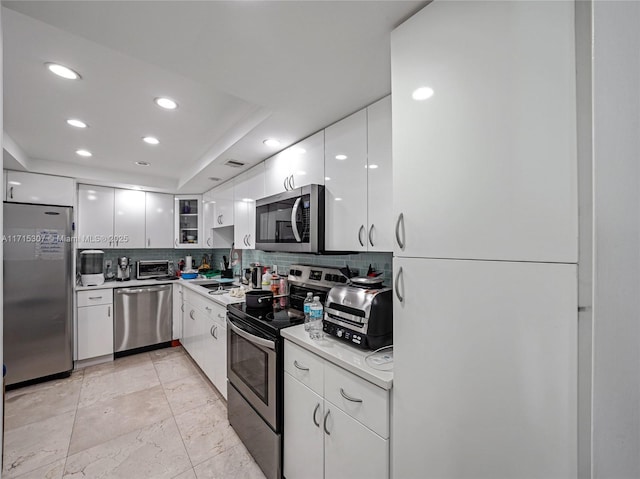kitchen featuring decorative backsplash, white cabinets, stainless steel appliances, light countertops, and recessed lighting