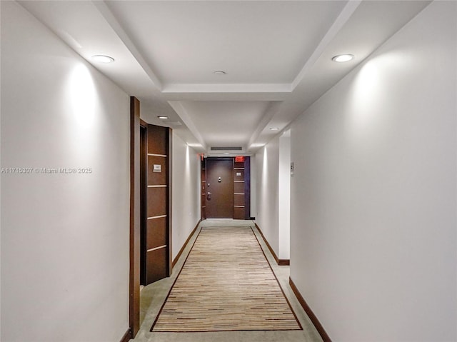 hallway featuring a raised ceiling, recessed lighting, and baseboards