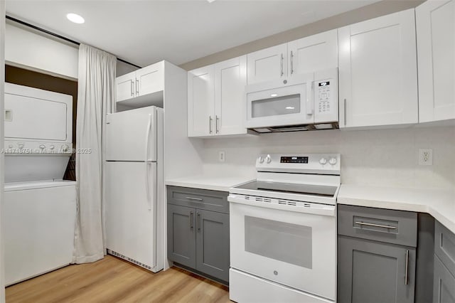 kitchen featuring gray cabinets, stacked washing maching and dryer, white cabinets, and white appliances