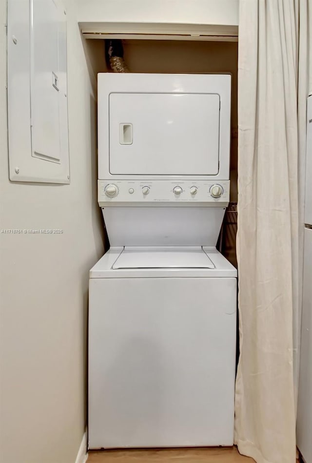 clothes washing area with electric panel and stacked washer and dryer