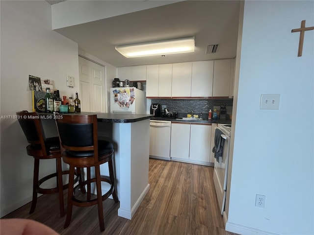 kitchen featuring white appliances, visible vents, dark countertops, a kitchen breakfast bar, and a peninsula