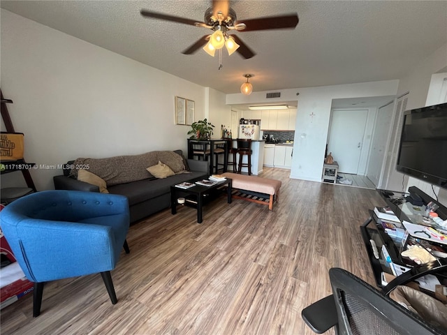 living room with a textured ceiling, ceiling fan, light wood-type flooring, and visible vents