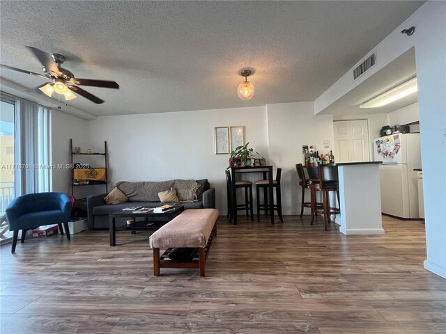 living room featuring wood-type flooring, ceiling fan, and a textured ceiling