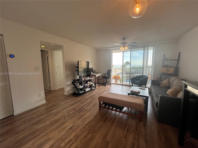 living room featuring a ceiling fan, expansive windows, baseboards, and wood finished floors