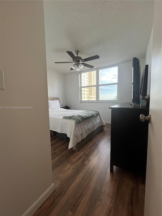 bedroom with a ceiling fan, a textured ceiling, baseboards, and dark wood-type flooring