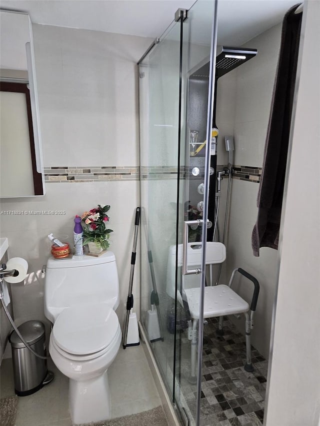 bathroom featuring tile patterned floors, a shower with shower door, tile walls, and toilet