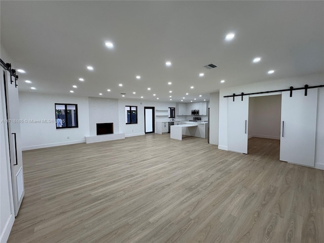 unfurnished living room with a large fireplace, a barn door, and light wood-type flooring