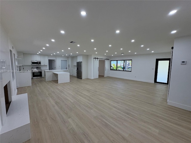 unfurnished living room with light wood-type flooring, a barn door, and sink