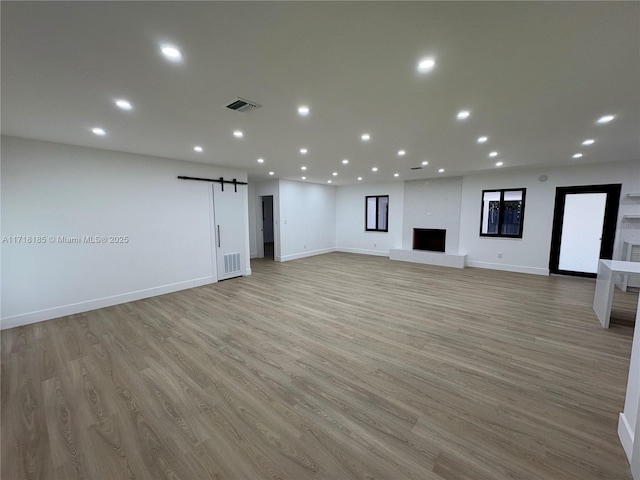 unfurnished living room featuring a barn door, a large fireplace, and light wood-type flooring