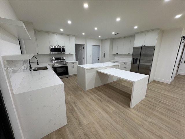 kitchen with a center island, sink, stainless steel appliances, white cabinets, and light wood-type flooring