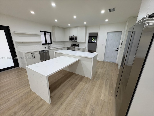 kitchen featuring appliances with stainless steel finishes, light wood-type flooring, a kitchen island, sink, and white cabinetry