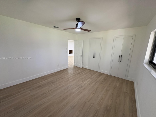 unfurnished bedroom featuring ceiling fan, wood-type flooring, and multiple closets