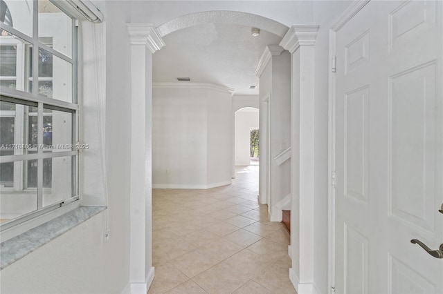 hallway with decorative columns, crown molding, light tile patterned flooring, and a textured ceiling