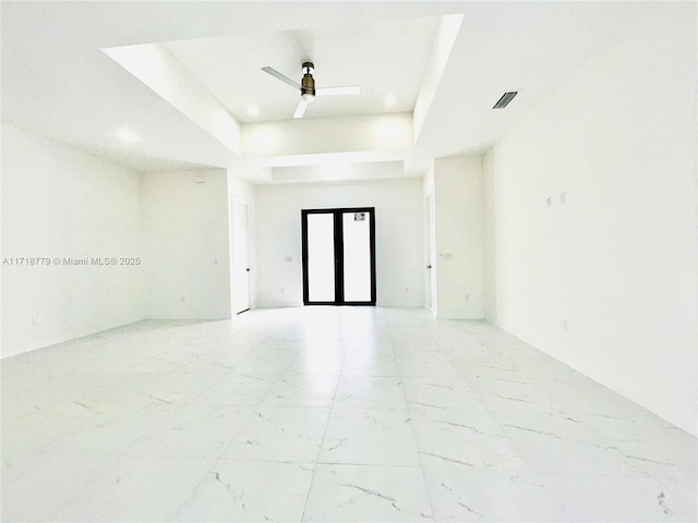 empty room with ceiling fan and a tray ceiling