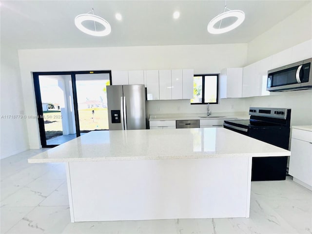 kitchen with a center island, sink, appliances with stainless steel finishes, decorative light fixtures, and white cabinetry