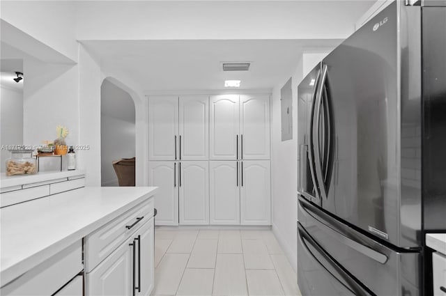 kitchen featuring stainless steel fridge, white cabinetry, and light tile patterned flooring