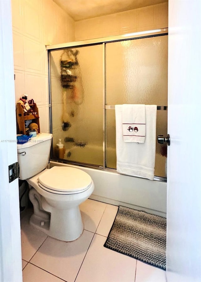 bathroom with combined bath / shower with glass door, tile patterned flooring, and toilet