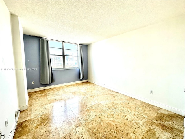 spare room featuring a textured ceiling and baseboards