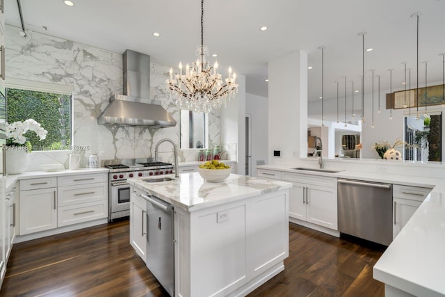 kitchen with wall chimney range hood, sink, appliances with stainless steel finishes, an island with sink, and light stone countertops