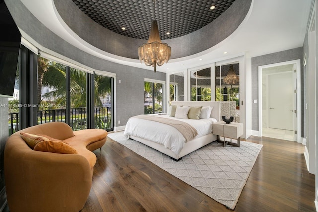 bedroom featuring access to exterior, dark hardwood / wood-style floors, a towering ceiling, an inviting chandelier, and a tray ceiling