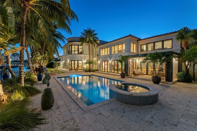 pool at dusk featuring an in ground hot tub and a patio