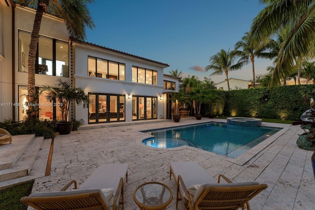 pool at dusk featuring an in ground hot tub and a patio