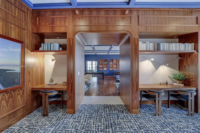 hallway featuring coffered ceiling and wood walls