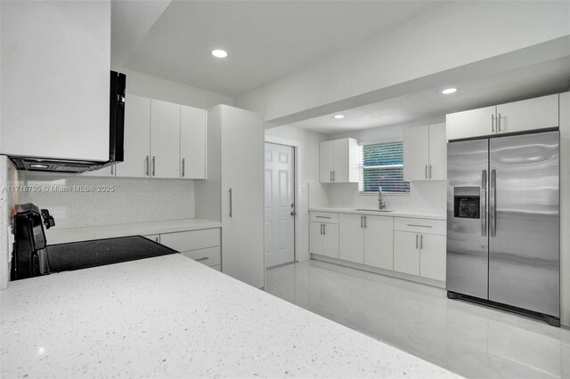 kitchen with white cabinets, stove, built in fridge, and sink