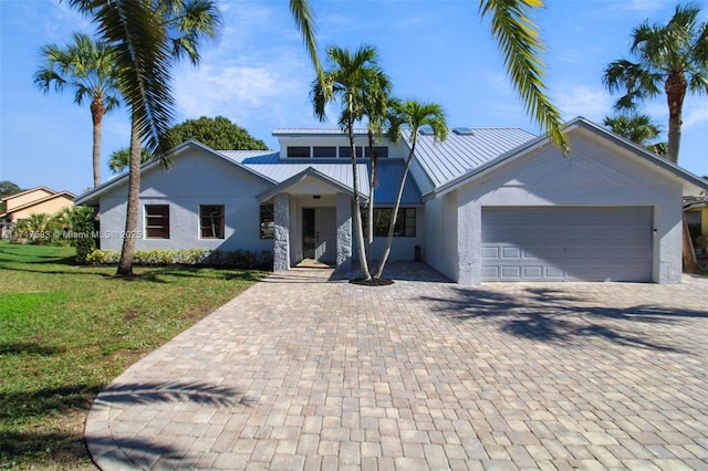 view of front of house with a front lawn, stucco siding, metal roof, decorative driveway, and a garage