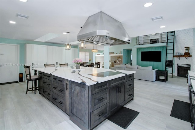 kitchen with a large fireplace, island exhaust hood, pendant lighting, a spacious island, and black electric stovetop