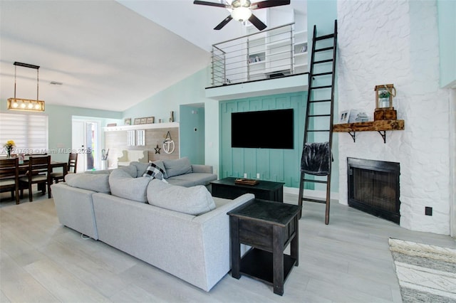 living room featuring a fireplace, light hardwood / wood-style floors, high vaulted ceiling, and ceiling fan