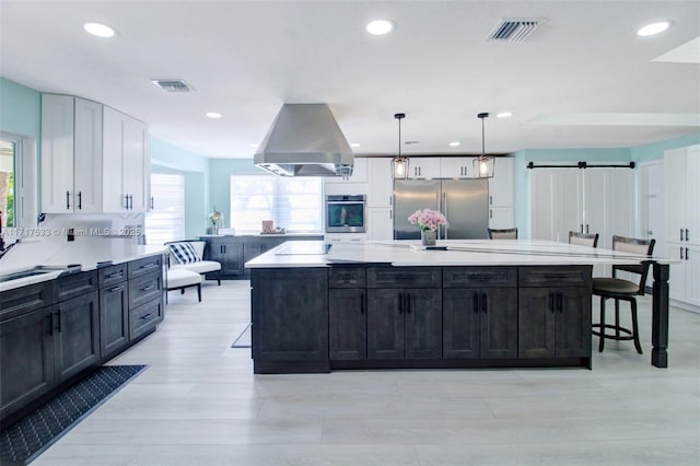 kitchen with high end refrigerator, a breakfast bar area, a barn door, decorative light fixtures, and island exhaust hood