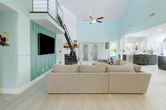 living room with ceiling fan, light hardwood / wood-style flooring, a high ceiling, and french doors