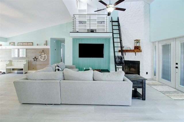 living room with ceiling fan, a stone fireplace, high vaulted ceiling, and french doors