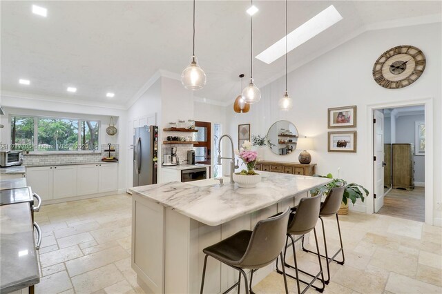 kitchen with light stone countertops, a skylight, ornamental molding, stone tile flooring, and stainless steel fridge