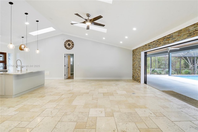 unfurnished living room featuring high vaulted ceiling, a ceiling fan, stone tile flooring, a skylight, and baseboards