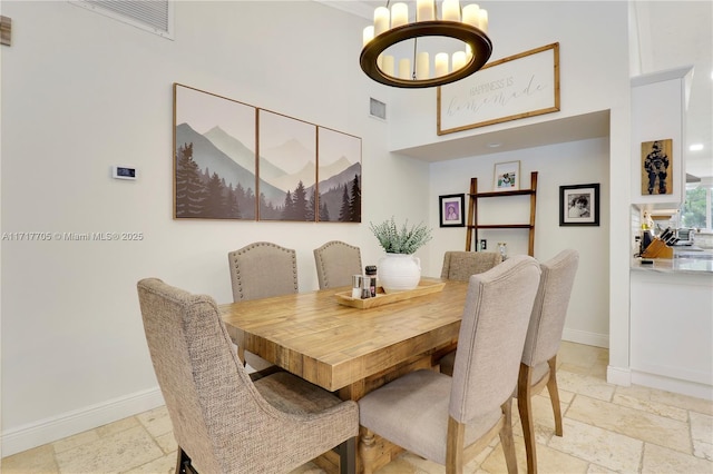 dining space featuring stone tile floors, baseboards, visible vents, an inviting chandelier, and a towering ceiling