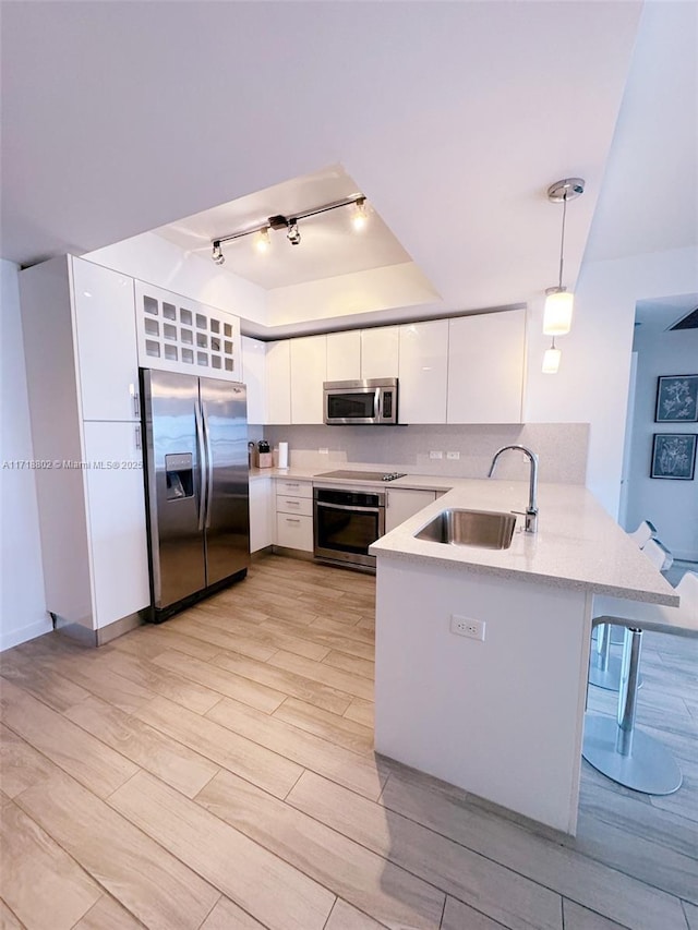 kitchen with kitchen peninsula, stainless steel appliances, sink, decorative light fixtures, and white cabinetry