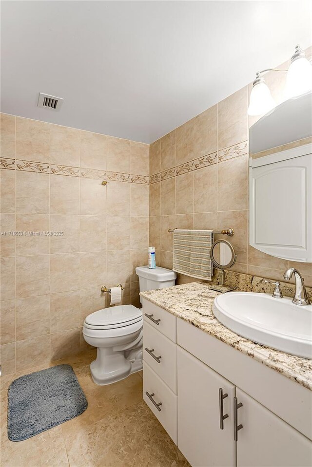 bathroom featuring tile patterned floors, vanity, toilet, and tile walls