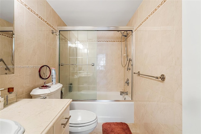 full bathroom with combined bath / shower with glass door, tile patterned floors, vanity, tile walls, and toilet