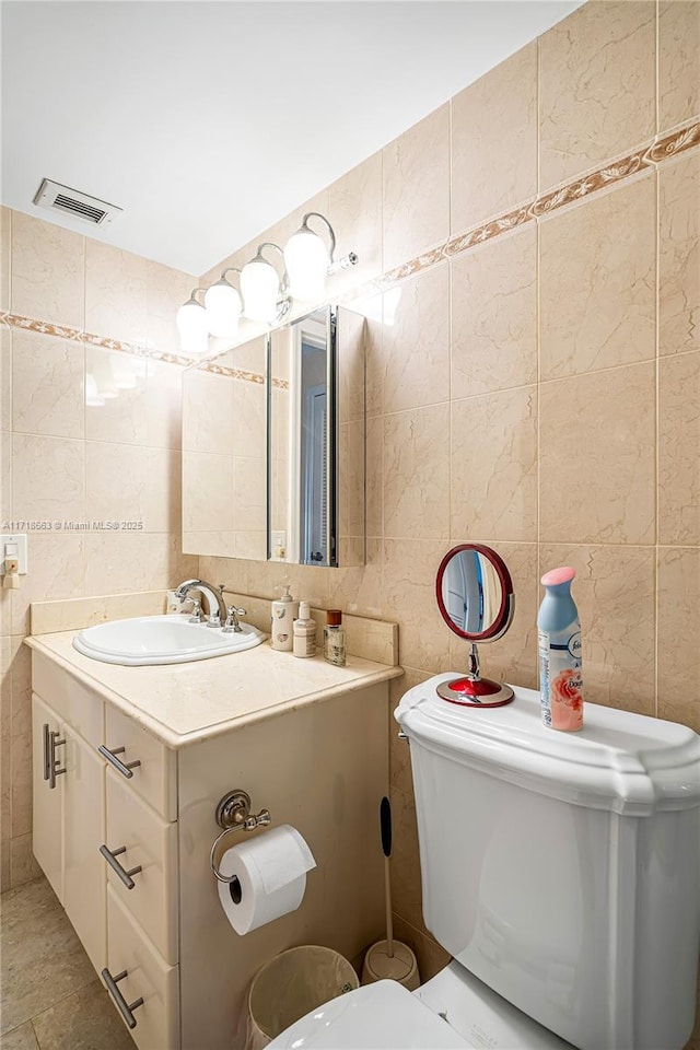 bathroom featuring tile patterned flooring, vanity, toilet, and tile walls